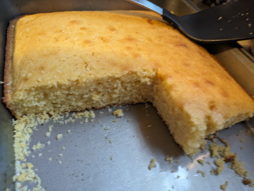 Cornbread in a metal baking pan. At least five pieces have already been cut and taken away. Nice crumb!